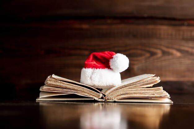 Libro viejo y sombrero de Navidad en mesa de madera