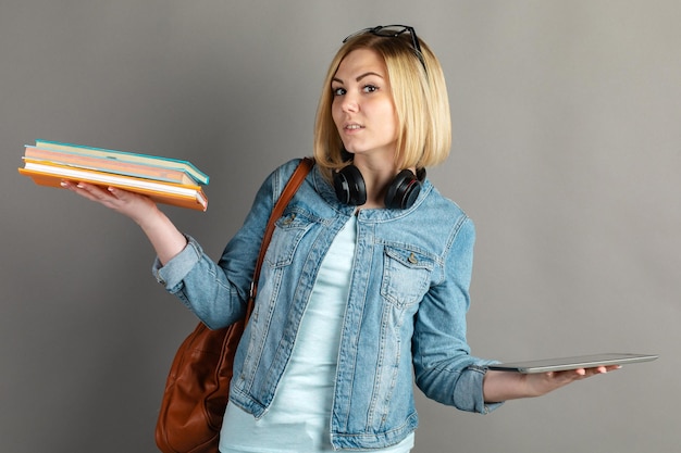 Libro vs libro electrónico Chica estudiante sosteniendo un libro de texto tradicional y leyendo libros electrónicos aislados en fondo gris Elija entre libros en papel y dispositivos de aprendizaje electrónico El concepto de educación moderna