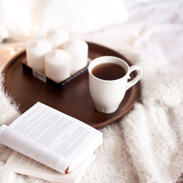 Libros abiertos, velas y una taza de té en una bandeja de madera en la cama Buenos días Tiempo libre