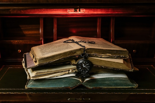 Libros antiguos apilados con un reloj de bolsillo