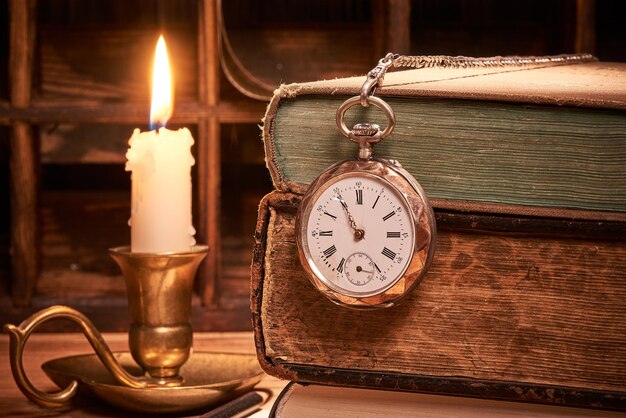 Foto libros antiguos con reloj de bolsillo antiguo a la luz de las velas