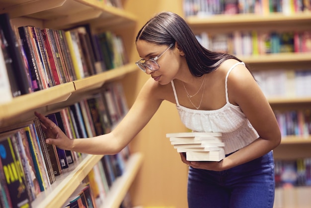 Foto libros de la biblioteca y mujer leyendo un libro impreso para su educación y aprendizaje universitario o universitario conocimiento de los jóvenes becarios de la generación z en el estante estudiando para un examen o prueba de proyecto de inglés