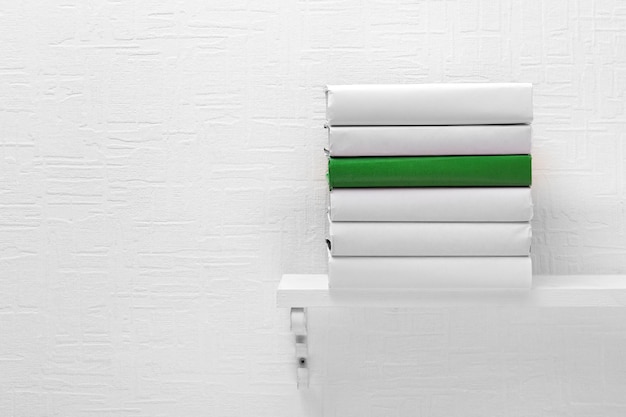 Foto libros en blanco y uno verde en el estante sobre fondo de papel pintado blanco