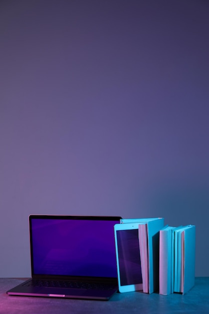 Libros con una computadora portátil en un fondo azul-rosado claro
