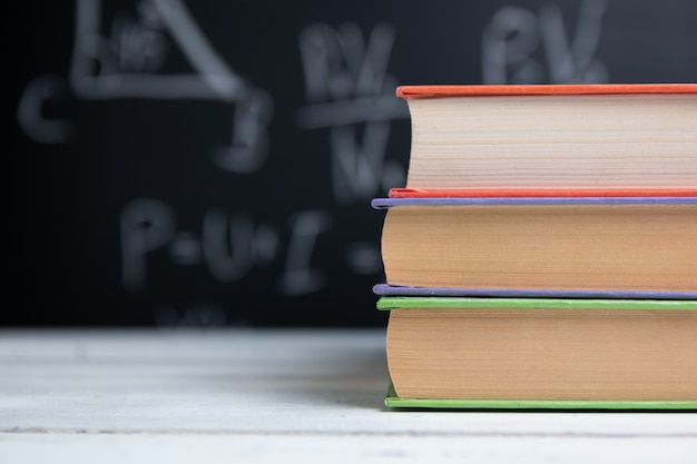 Libros escolares en mesa blanca en pizarra