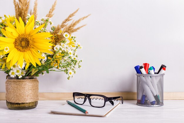 Libros, gafas, marcadores y un ramo de flores en un jarrón sobre blanco