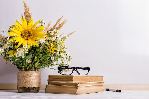 Libros, gafas, marcadores y un ramo de flores en un jarrón sobre pizarra blanca