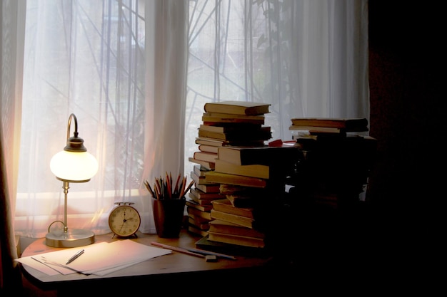 Libros y lámpara iluminada en el escritorio de casa