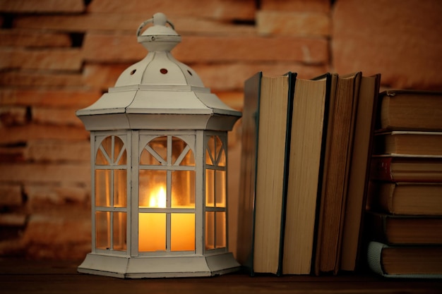 Libros y linterna decorativa sobre fondo de mesa y pared de ladrillo