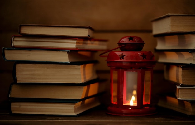 Libros y linterna decorativa sobre mesa y fondo de tablones de madera.