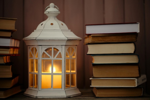Libros y linterna decorativa sobre mesa y fondo de tablones de madera.