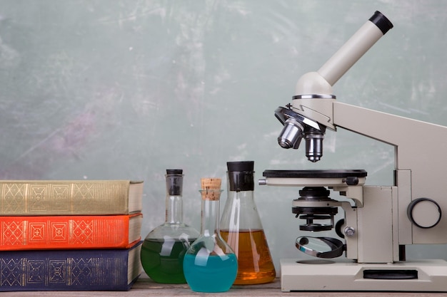 Libros de matraces químicos y microscopio en el escritorio sobre fondo verde