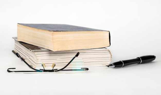 Libros pluma y gafas sobre un fondo blanco.