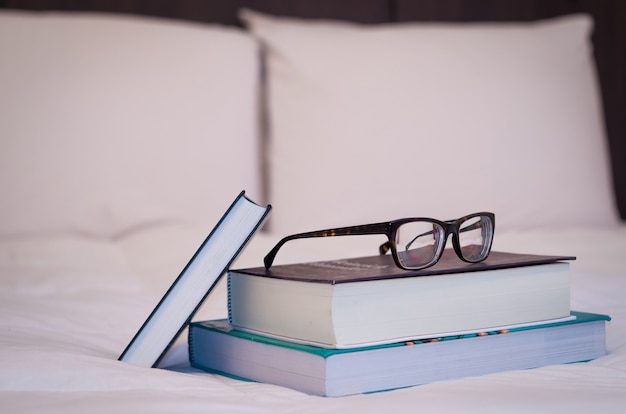 Foto libros sobre la cama blanca, vasos encima.