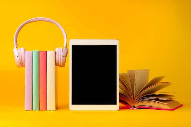 Libros con tableta digital y auriculares sobre fondo amarillo