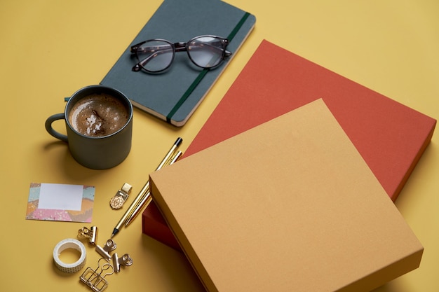 Libros, taza de café, gafas de lectura, bolígrafo y lápices en amarillo.