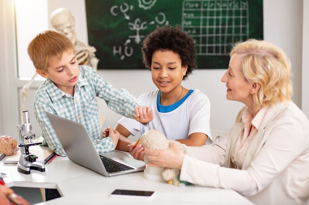 Foto lição da escola. professora alegre e positiva conversando com seu aluno enquanto explica o material