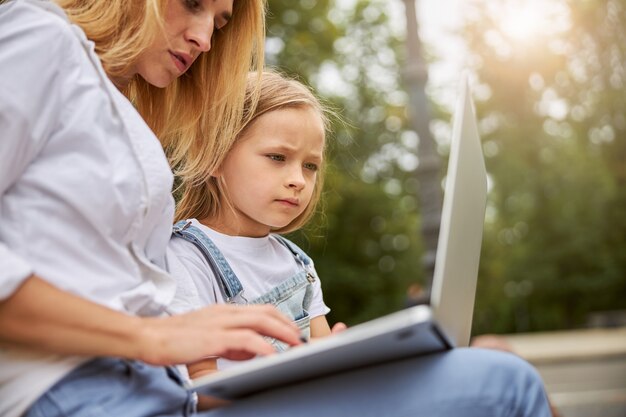 Lição de audição e aprendizagem de garotinha inteligente e fofa no laptop enquanto a mãe conta detalhes