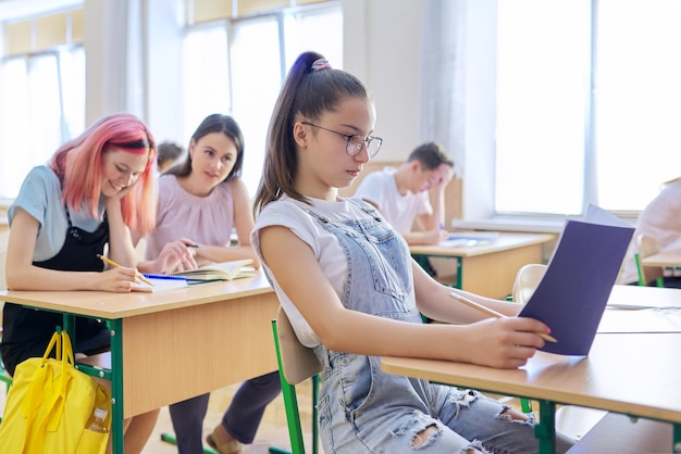 Lição na classe dos filhos adolescentes, na frente garota de 13, 14 anos sentada na mesa. educação, escola, faculdade, conceito de crianças em idade escolar