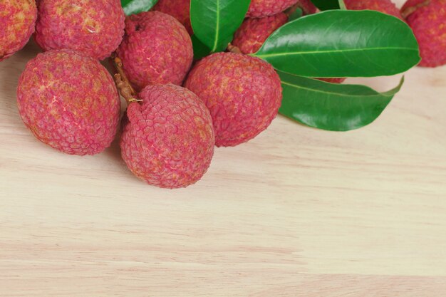 Lichi rojo fresco de la piel con las hojas en fondo de madera con el espacio de la copia.