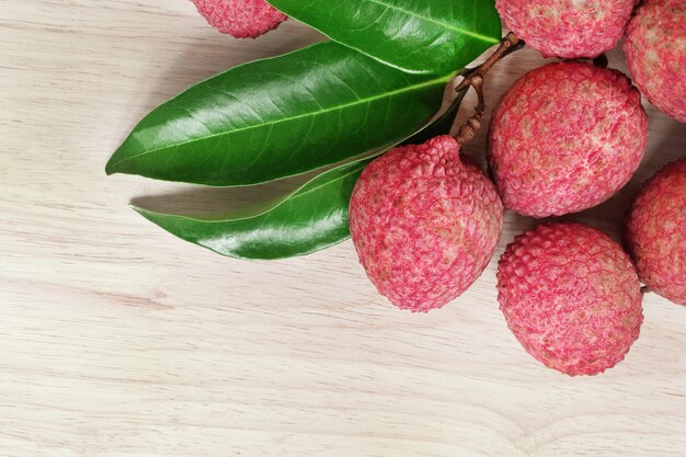 Lichi vermelho fresco da pele com as folhas no fundo de madeira com espaço da cópia.