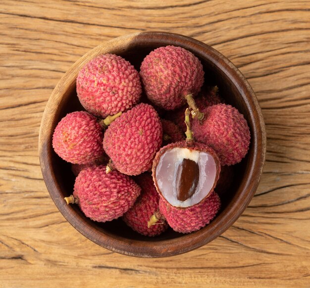 Lichias em uma tigela com frutas cortadas sobre a mesa de madeira.