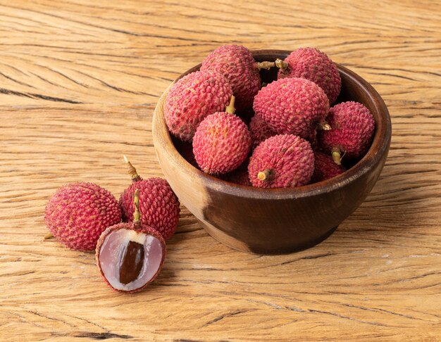 Lichis en un bol con fruta cortada sobre una mesa de madera.