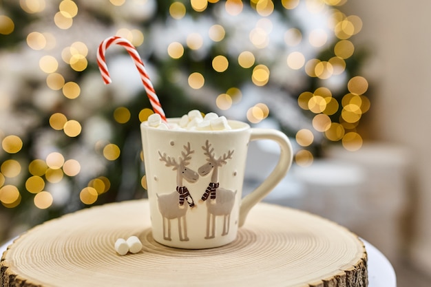 Lichterkette Hintergrund, heißer Kakao mit Marshmallows, weiße Tasse mit Hirsch auf einem Holzschnitt zu Hause während der Weihnachts- und Neujahrsferien. Weichzeichner-Bokeh.