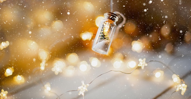 Foto lichterketten in einem glas mit weihnachtsbaum und schnee nahaufnahme auf einer warmen gemütlichen stimmung mit goldener girlande. weihnachten und neujahr, festliche dekoration, kopienraum. weihnachtshintergrund