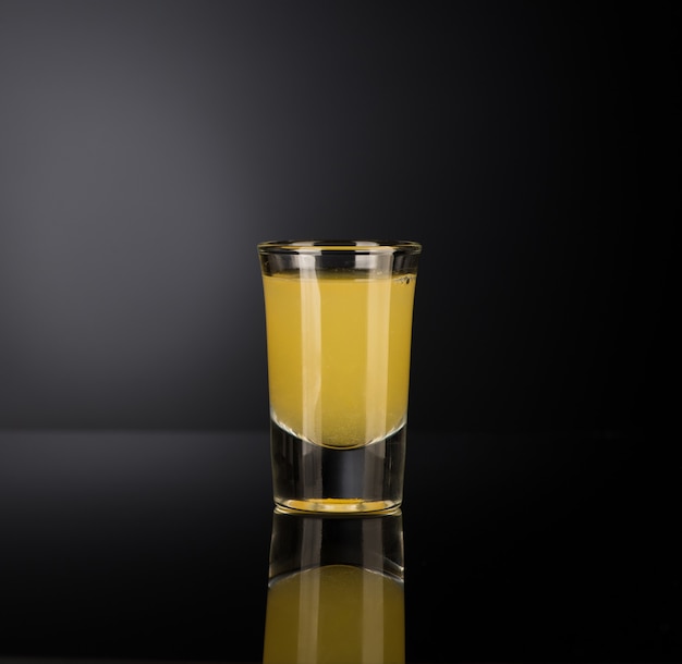 Licor alcohólico amarillo en un vaso de chupito aislado sobre fondo oscuro con retroiluminación