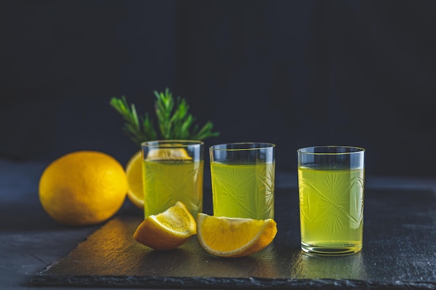 Licor de bebida de alcohol de limón casero italiano tradicional limoncello con trozos de hierba de limón y romero sobre superficie de hormigón de piedra negra