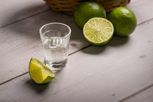 Foto licor de caña de azúcar en un vaso pequeño sobre una mesa de madera con limones