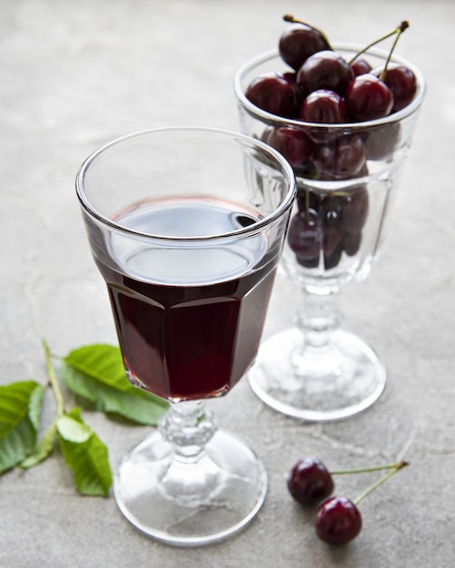 Licor de cereza en un vaso y fruta fresca sobre un fondo de hormigón gris