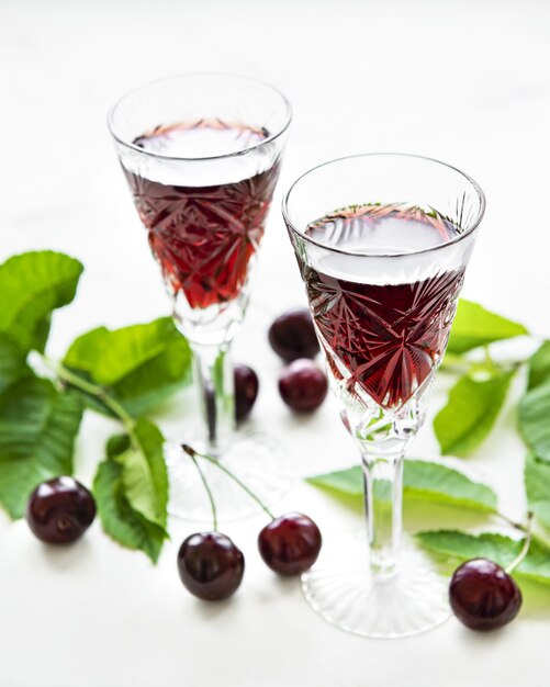 Licor de cereza en un vaso y fruta fresca sobre fondo de mármol blanco