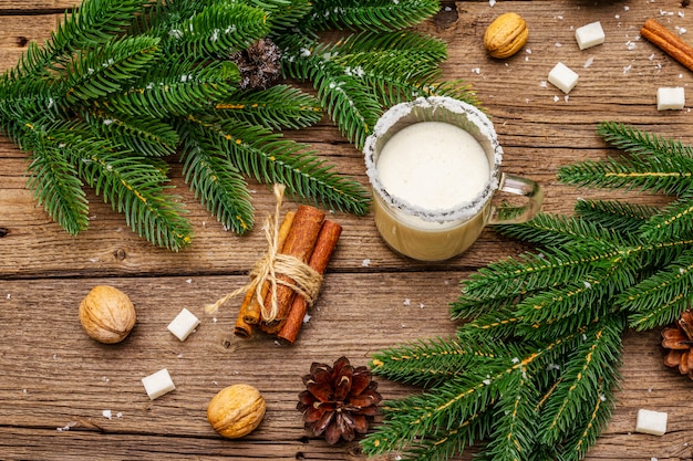 Licor de ponche de Navidad o cóctel de cola de mono. Bebida clásica de invierno en taza de vidrio, decoraciones de Navidad. Ramas de hoja perenne, canela, nueces, azúcar.