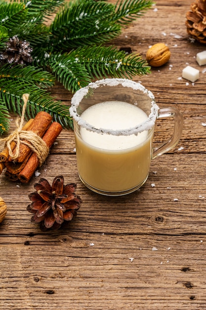 Licor de ponche de Navidad o cóctel de cola de mono. Bebida clásica de invierno en taza de vidrio, decoraciones de Navidad. Ramas de hoja perenne, canela, nueces, azúcar.