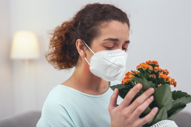 Lidar com alergias. Jovem com aparência doente usando uma máscara respiratória de proteção que a mantém protegida de uma flor que causa suas alergias sazonais