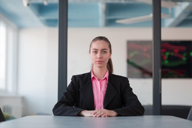 Líder feminina bem-sucedida de terno com camisa rosa, sentada em um escritório de vidro moderno com um sorriso determinado Conceito de negócios e o sucesso dos jovens em empresas on-line modernas