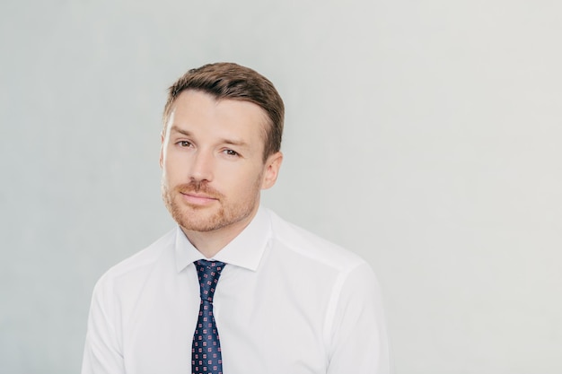 El líder masculino exitoso con una mirada segura piensa en la cooperación con su pareja y quiere mejorar su situación financiera, usa camisa blanca elegante y corbata aislada sobre fondo blanco