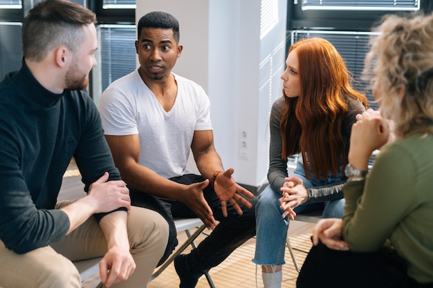 Líder masculino profesional afroamericano explicando nuevas estrategias al joven equipo empresarial creativo, durante la lluvia de ideas en la sala de reuniones. Hombre de negocios discutiendo el trabajo con el equipo en la sala de juntas.