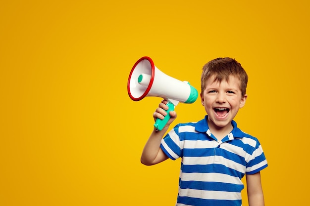 Líder de niño alegre hablando en megáfono y sonriendo mientras está de pie contra el fondo amarillo
