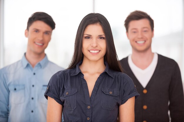 Foto líder real. atractiva mujer joven sonriendo mientras dos hombres de pie detrás de ella