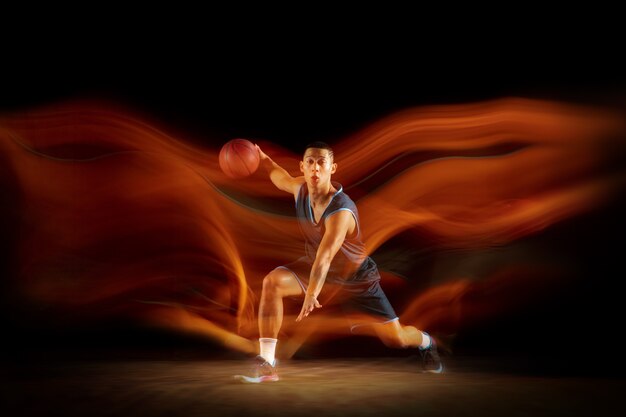 Liderazgo. Joven jugador de baloncesto del este asiático en acción y movimiento saltando en luz mixta sobre fondo oscuro de estudio. Concepto de deporte, movimiento, energía y estilo de vida dinámico y saludable.