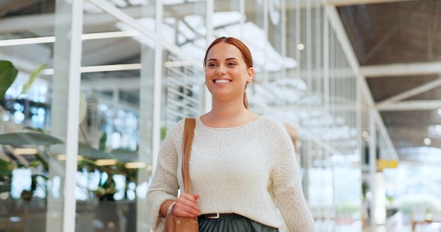 Liderazgo mujer de negocios y caminar en la oficina lista para comenzar las tareas de trabajo en la mañana Sonrisa de confianza y feliz empleada con bolso caminando en el pasillo o pasillo del vestíbulo del lugar de trabajo moderno
