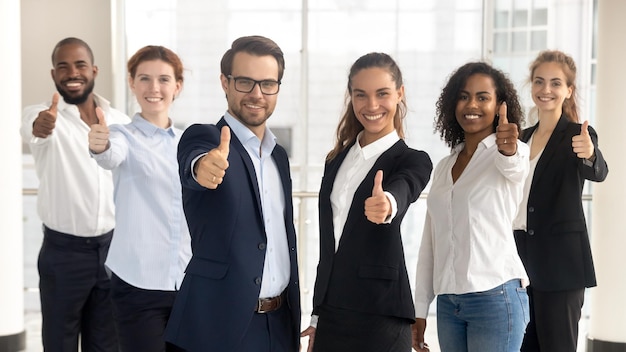 Líderes empresariales con empleados mostrando los pulgares hacia arriba mirando a la cámara