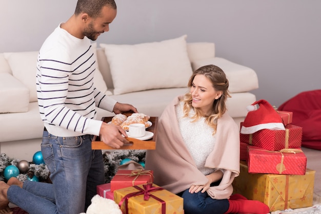 Liebe ausdrücken. netter hübscher angenehmer mann, der ein tablett hält und seiner frau ein frühstück anbietet, während er sich um sie kümmert