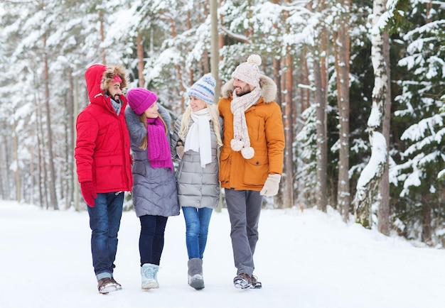 Liebe, Beziehung, Jahreszeit, Freundschaft und Menschenkonzept - Gruppe lächelnder Männer und Frauen, die im Winterwald spazieren und reden