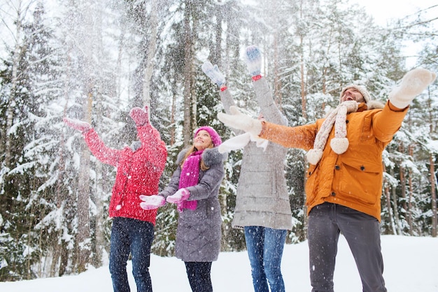 Liebe, Beziehung, Jahreszeit, Freundschaft und Menschenkonzept - Gruppe lächelnder Männer und Frauen, die Spaß haben und im Winterwald mit Schnee spielen