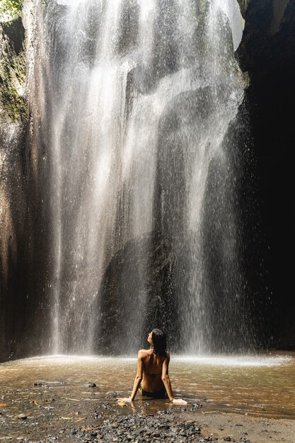 Liebe diesen Ort. Schlanke Frau sitzt vor Wasserfall und schaut nach oben in den Himmel