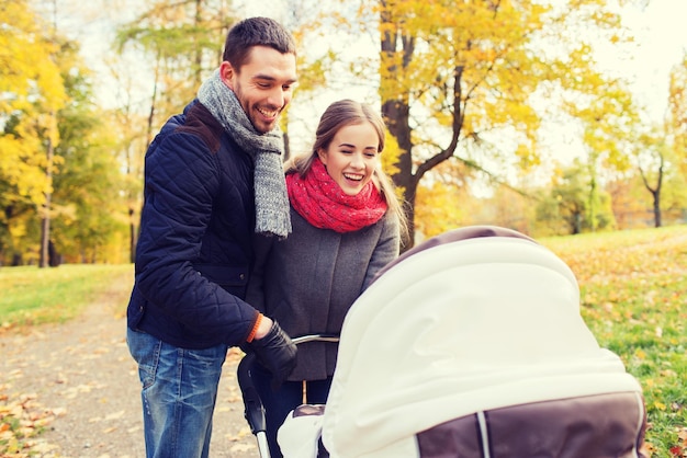 Liebe, Elternschaft, Familie, Jahreszeit und Personenkonzept - lächelndes Paar mit Kinderwagen im Herbstpark